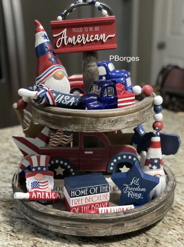 Playful 4th of July tray with gnome figures, vintage red and blue trucks, patriotic signs, and a 'Proud to be an American' plaque.