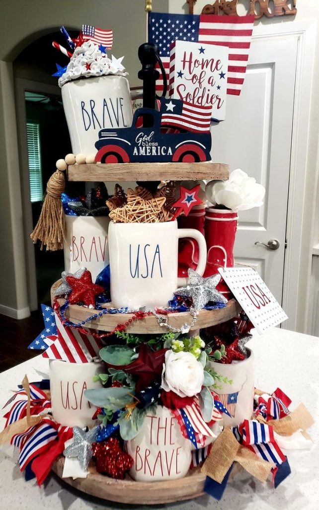 Full and festive three-tiered tray wrapped in ribbons, with 'Home of a Soldier' sign, USA mugs, and lots of patriotic decor.