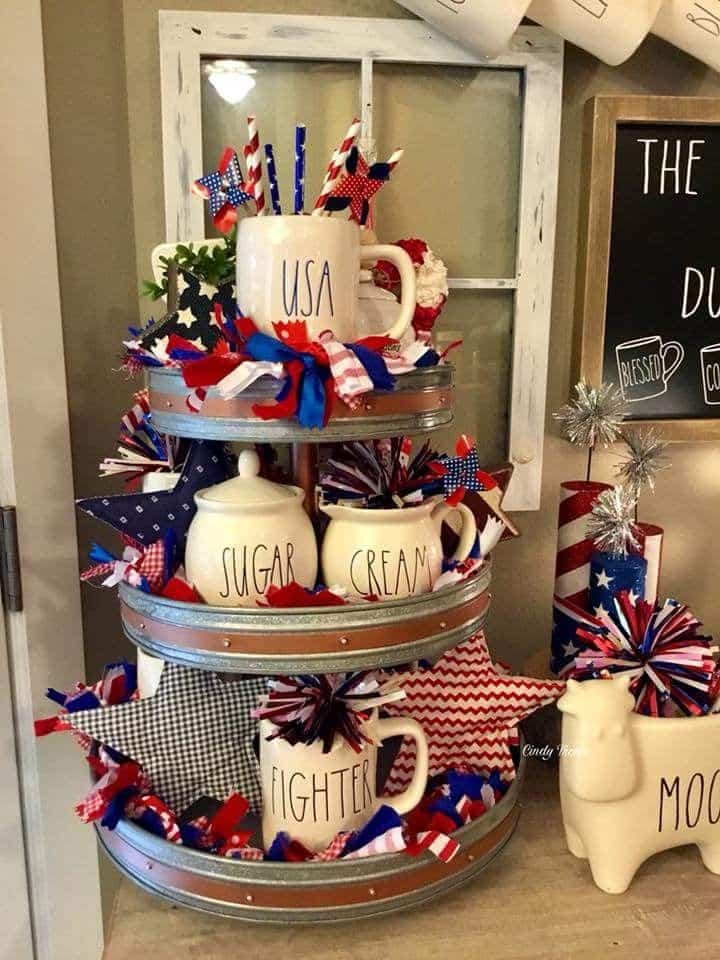 Rae Dunn-inspired kitchen tray with labeled jars, pinwheels, paper stars, and layers of ribbon in red, white, and blue.