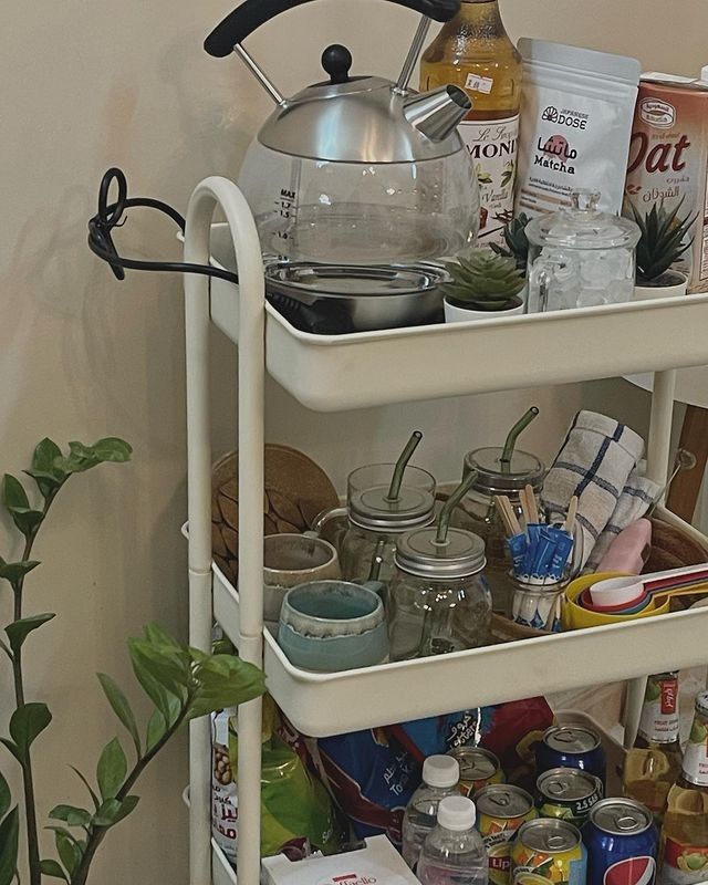 Rolling cart matcha bar setup with glass kettle, oat milk, syrups, mason jars, and matcha accessories, organised on three tiers with plants for a cosy feel.
