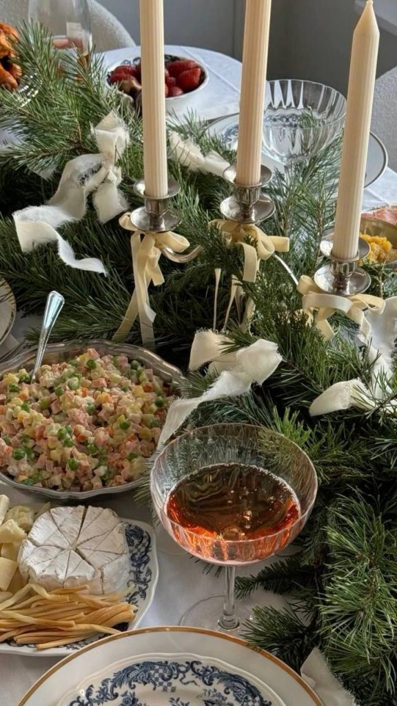 Christmas table with evergreen garland, ivory ribbons, and tall candles.