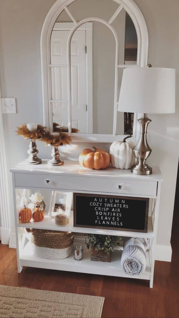 Bright white console table with orange pumpkins, gold candle wreaths, and letterboard with autumn sayings