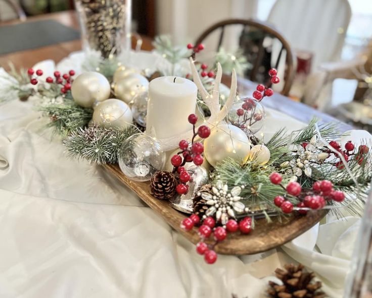 Elegant Christmas dough bowl centerpiece with white candle, silver ornaments, red berries, and white antlers.