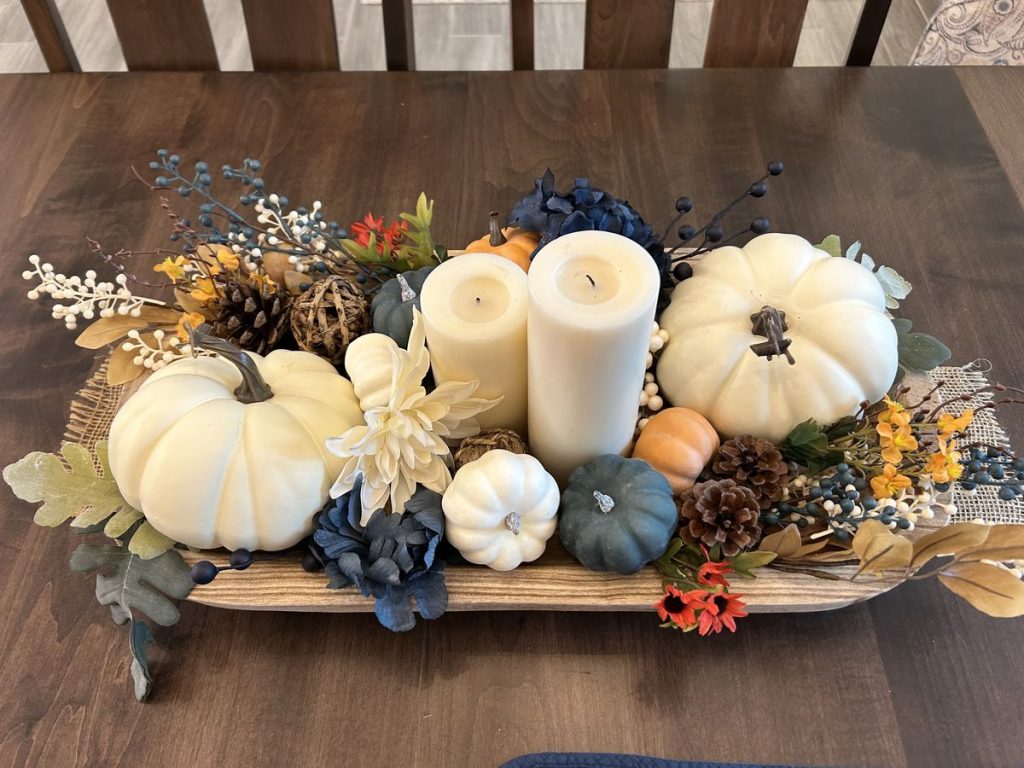 Autumn dough bowl centerpiece with navy and white pumpkins, white candles, and dark blueberries.