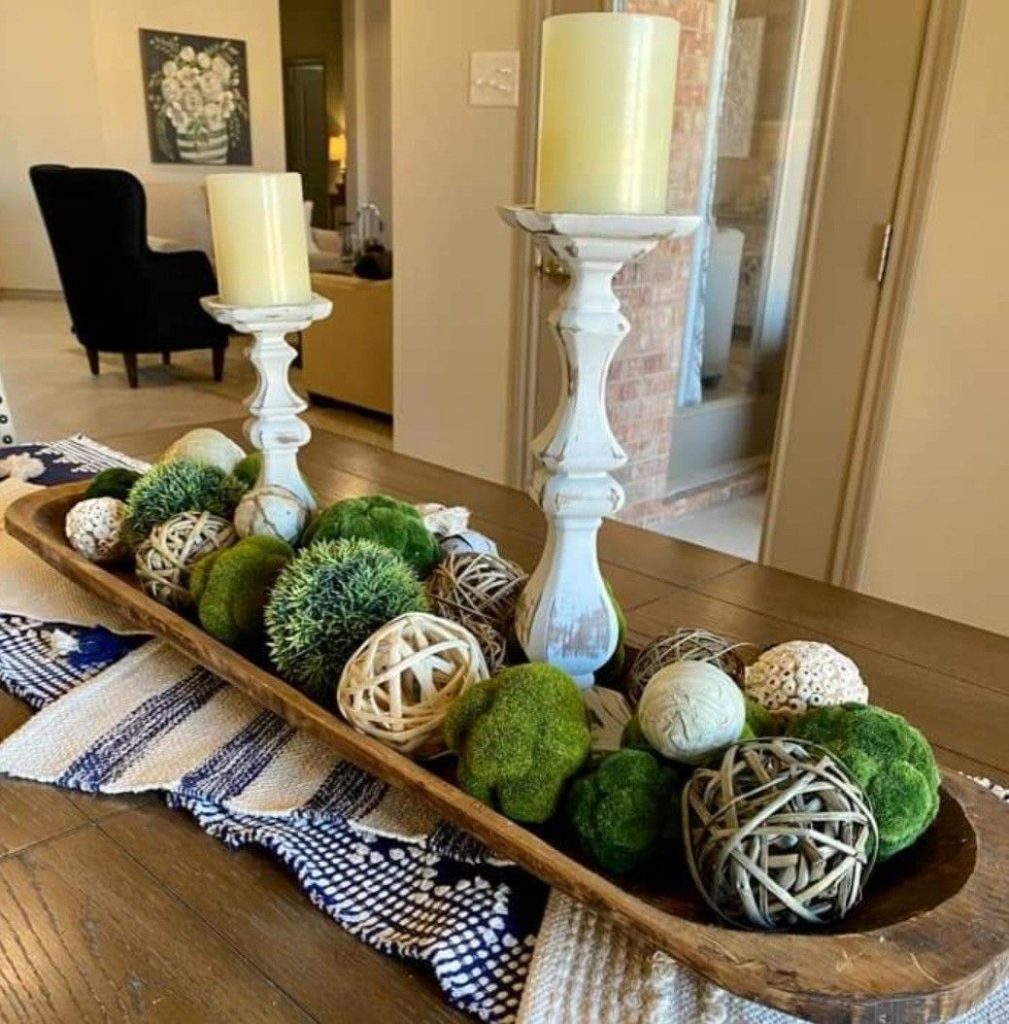 Extra long wooden dough bowl centerpiece with distressed white candleholders, moss balls, and rattan orbs.