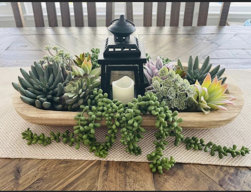 Modern dough bowl centerpiece with a black lantern, white candle, and vibrant mixed faux succulents.