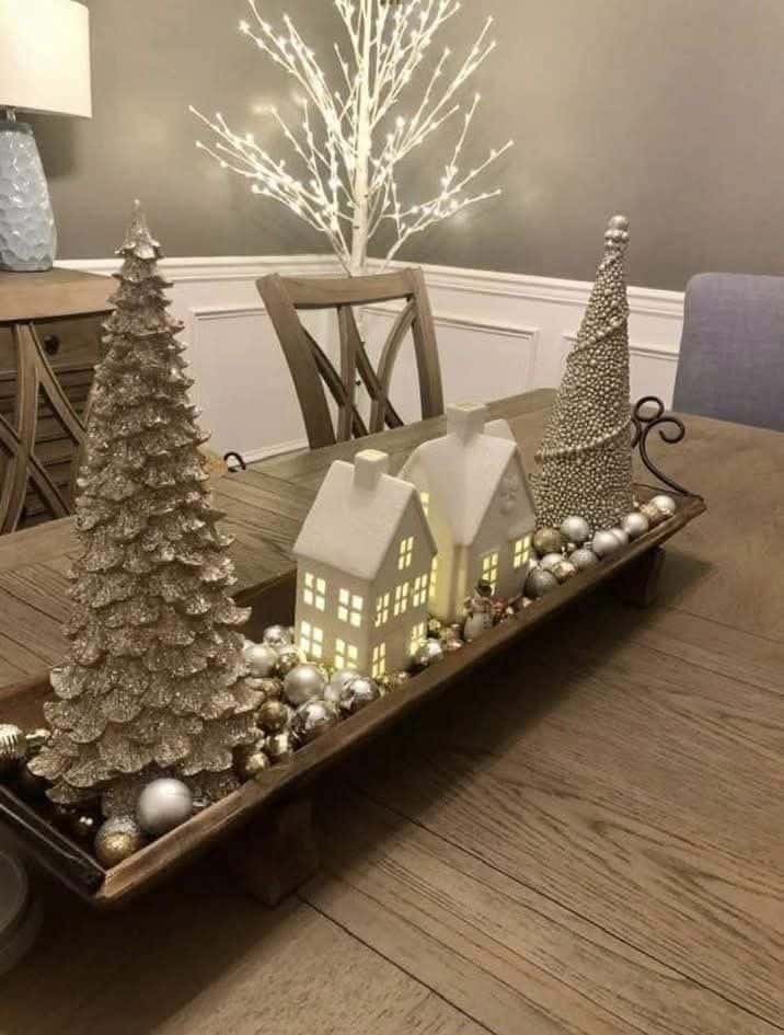 Long wooden dough bowl centerpiece with glittering gold and silver trees, white ceramic houses, and ornaments.