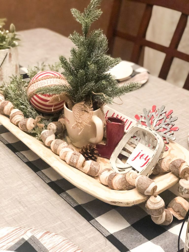 Whitewashed dough bowl Christmas centerpiece with a mini fir tree in a mug, red ornaments, and wood bead garland.