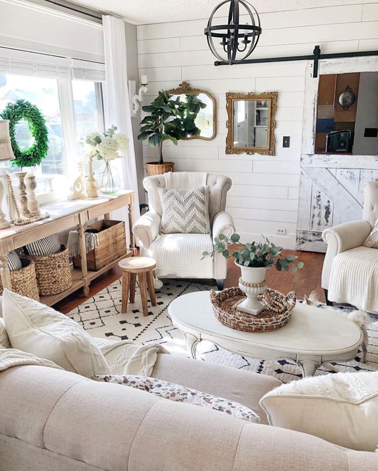 Light-filled modern farmhouse living room with white slip covered sofa, wooden console table with baskets, tufted armchair, and black orb chandelier.