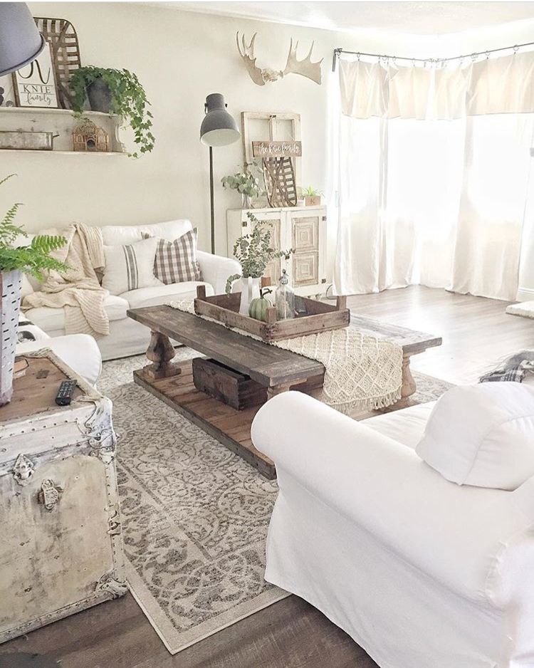 Light and airy farmhouse living room with white sofa, dark wooden coffee table, large floor lamp, and distressed white trunk side table.