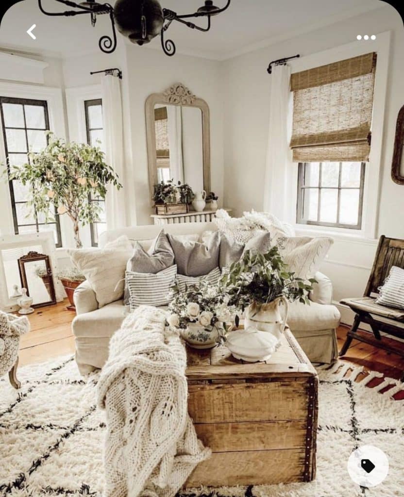 Highly textured farmhouse living room with chunky throw, shaggy rug, wooden trunk coffee table, and woven bamboo window blind.