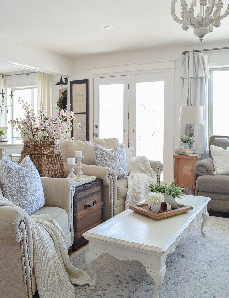 Serene farmhouse living room with two accent chairs, large white coffee table, vintage trunk side table, and French doors.