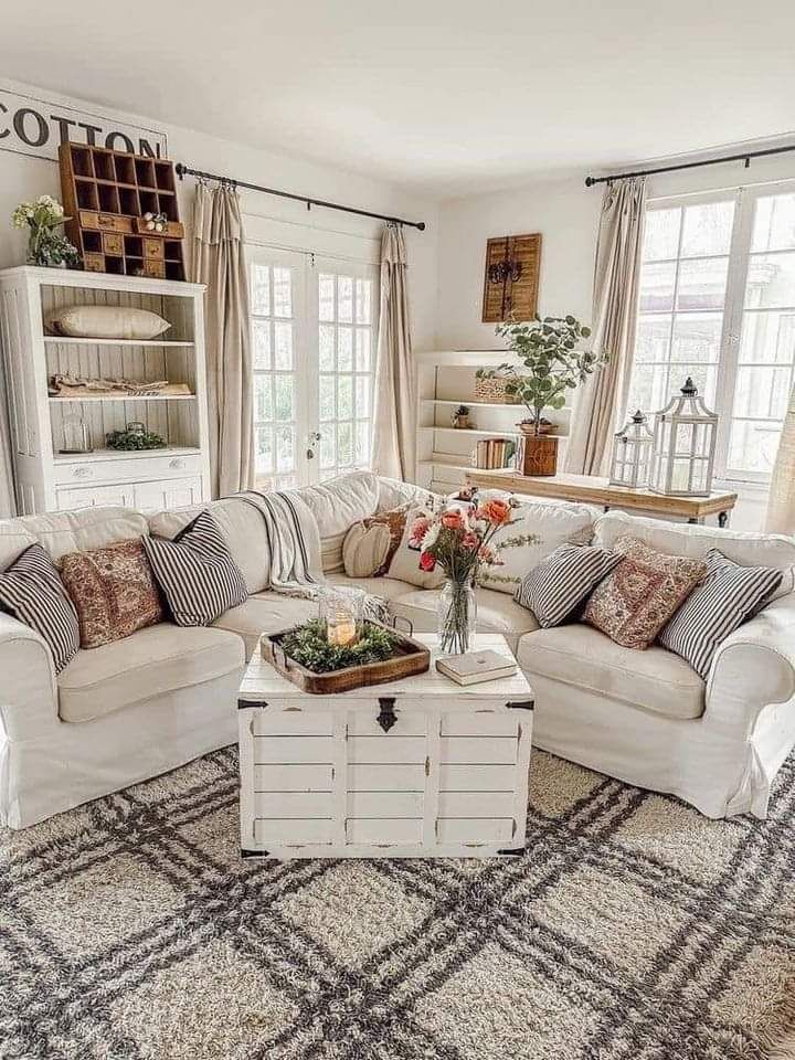 White farmhouse living room with sectional sofa, black and white plaid rug, white trunk coffee table, and rustic wooden shelving unit.