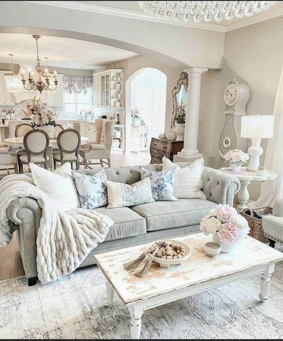 Luxury farmhouse living room with tufted gray sofa, floral cushions, distressed white coffee table, and large white floor clock.