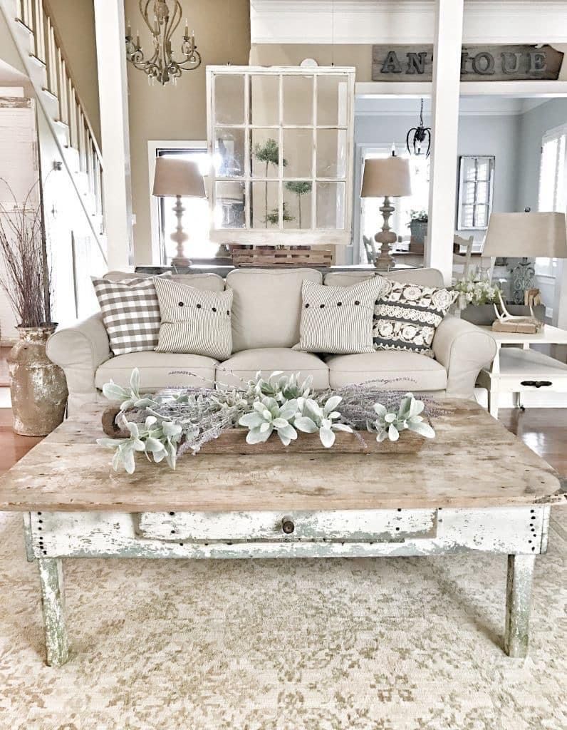 Rustic neutral farmhouse living room with distressed wood coffee table, ticking stripe cushions, and salvaged window pane art.