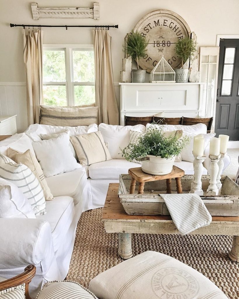Layered neutral farmhouse living room with white sectional, jute rug, oversized round wooden sign decor, and white candlesticks.