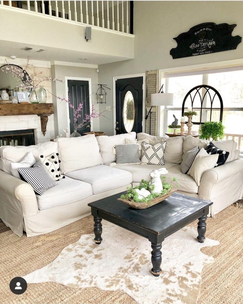 Black and white farmhouse living room with large white sectional, cowhide rug on jute rug, and black coffee table with carved legs.