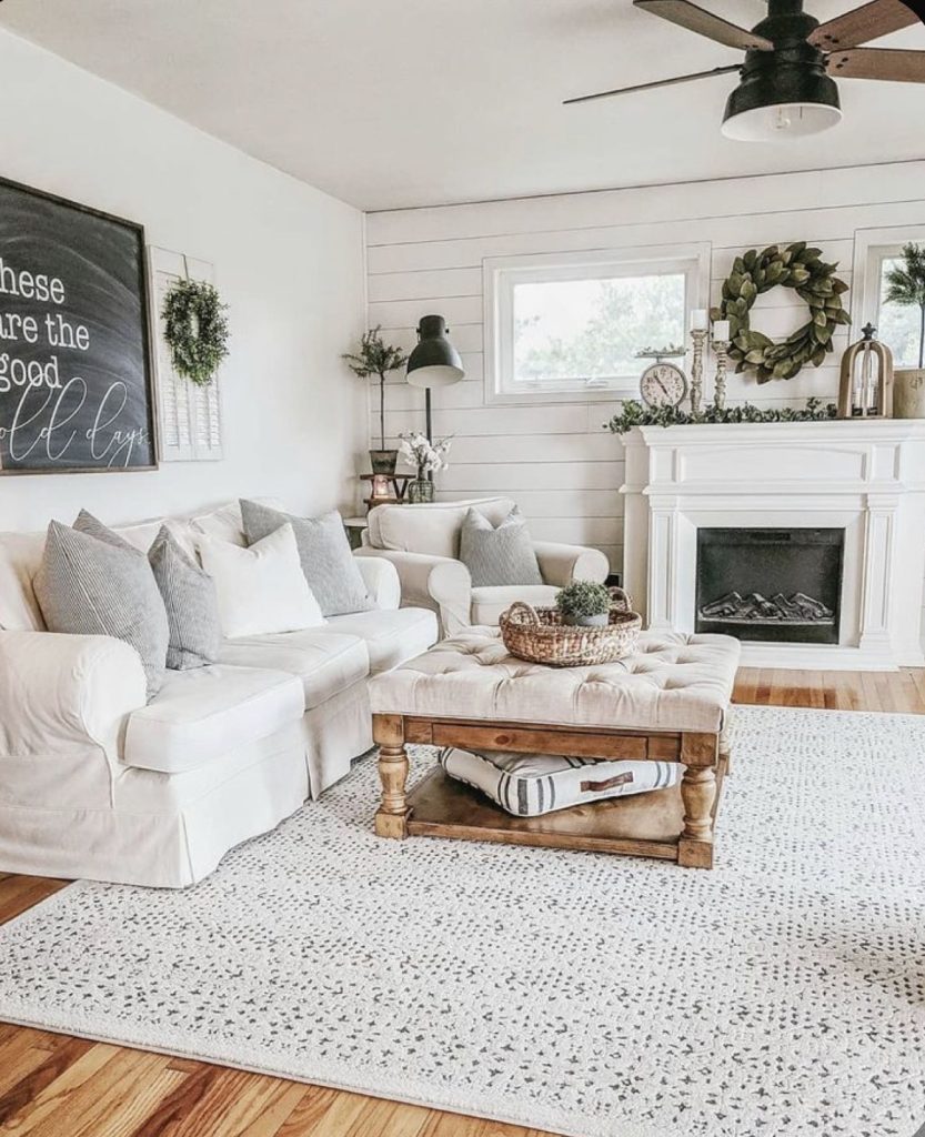 Classic farmhouse living room with ship lap fireplace, white sofa, tufted wood coffee table, and large chalkboard sign.