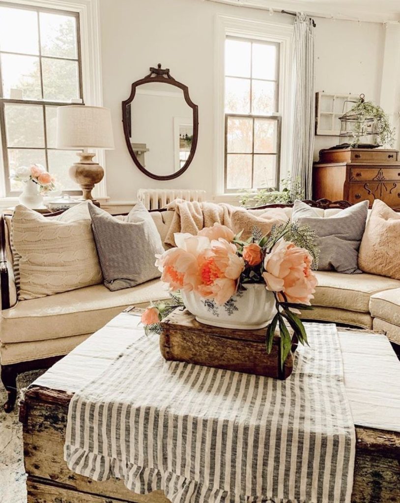 Elegant farmhouse living room with light sofa, peach cushions, antique mirror, and peach peony floral arrangement on a striped runner.