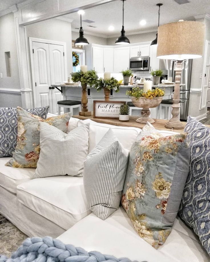 Open-plan farmhouse living room with white sectional sofa, blue and floral cushions, and wood console table separating living space from kitchen.
