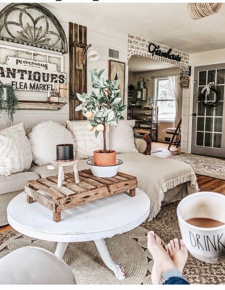 Rustic farmhouse living room with layered vintage signs, salvaged wood accents, and white coffee table with natural fiber rug.
