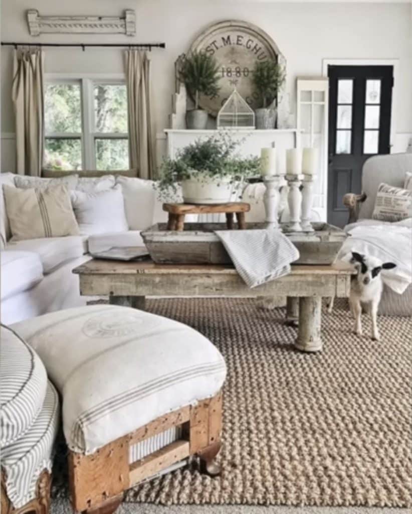 Vintage rustic farmhouse living room with white slip covered sofa, large antique wooden clock sign, and distressed wooden coffee table.