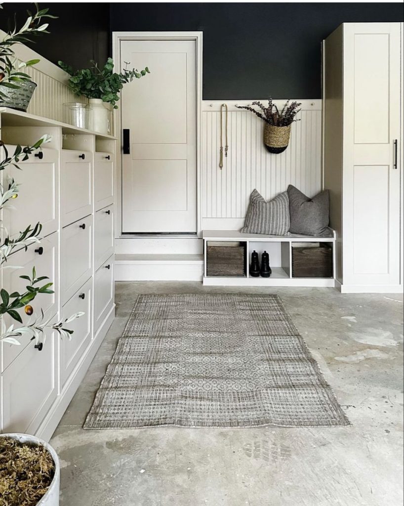Stylish garage entryway featuring white bead board, a bench nook with cushions, closed shoe cabinets, and a long patterned rug.