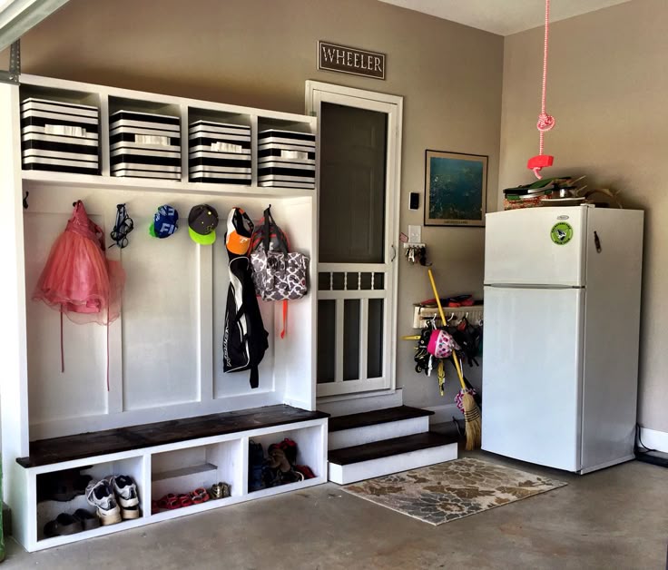 Garage entry with a built-in mud room bench with dark wood top and open cubbies for shoes, black and white striped storage bins, and a full-size refrigerator.