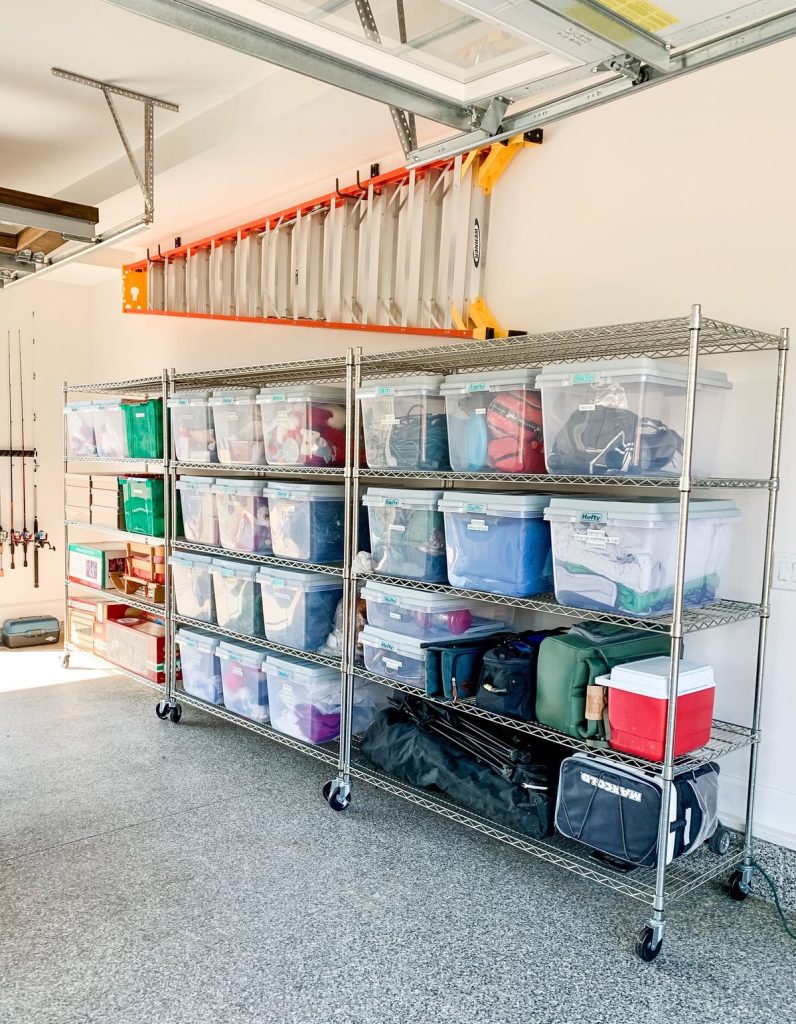 Heavy-duty chrome wire shelving units on wheels, stacked high with clear plastic storage tubs containing camping gear, blankets, and sports equipment.