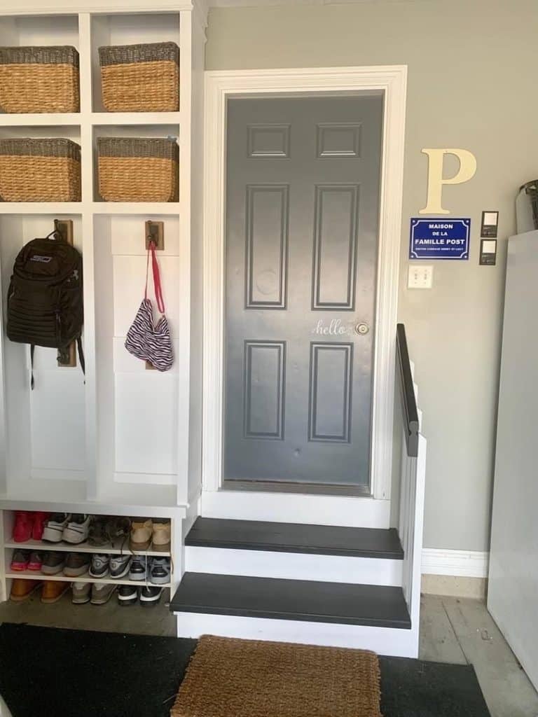 Small mud room area built into a garage entry, featuring a custom white cubby unit with woven baskets, a bench, and a dark gray entry door.