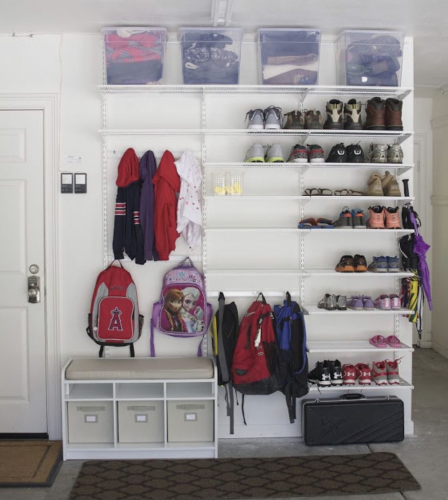 White wire shelving system used as a garage mud room with coat hooks, a small bench, and rows of shelves dedicated to storing shoes.