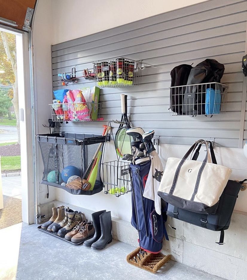 Garage wall with slat system used to organize sports gear including a golf bag, tennis rackets, boots, and mesh storage bins.