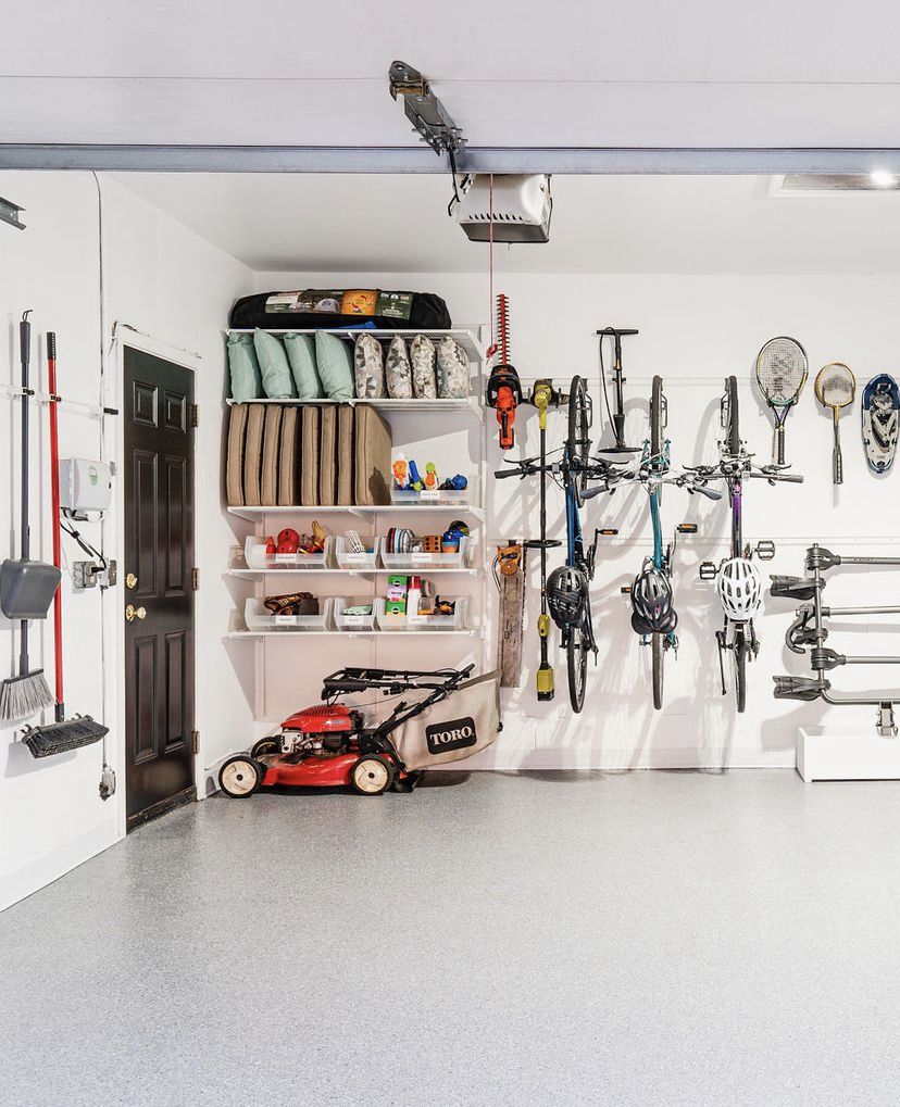 Clean, white garage space with light gray epoxy floor showing wall-mounted shelving for bins and vertical racks for bicycles and yard tools.