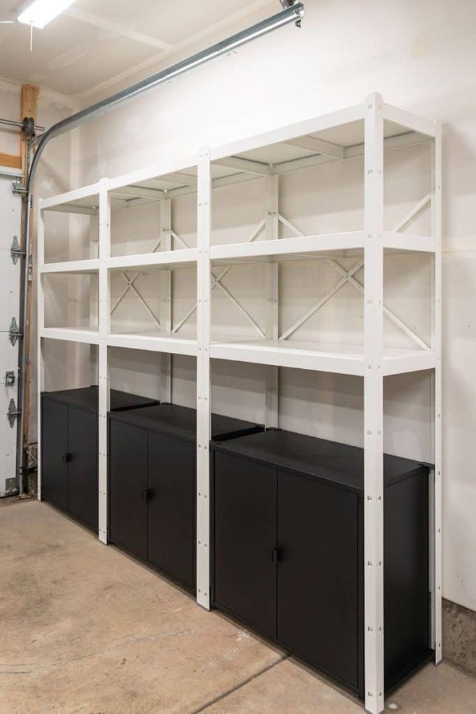 Modern industrial shelving in a garage featuring white metal frames over black closed storage cabinets, creating a clean, high-contrast look.