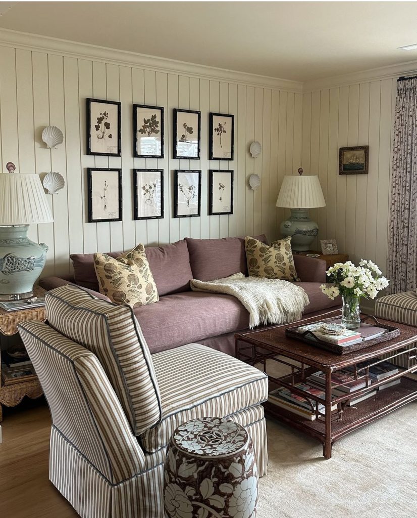 A grid of eight botanical prints in dark frames on a cream-paneled wall above a mauve sofa.