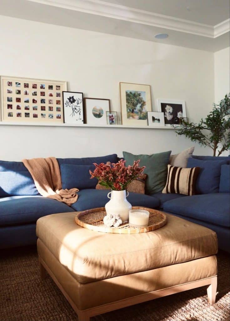 A very long white floating shelf above a blue sectional sofa with a diverse mix of art and photos.