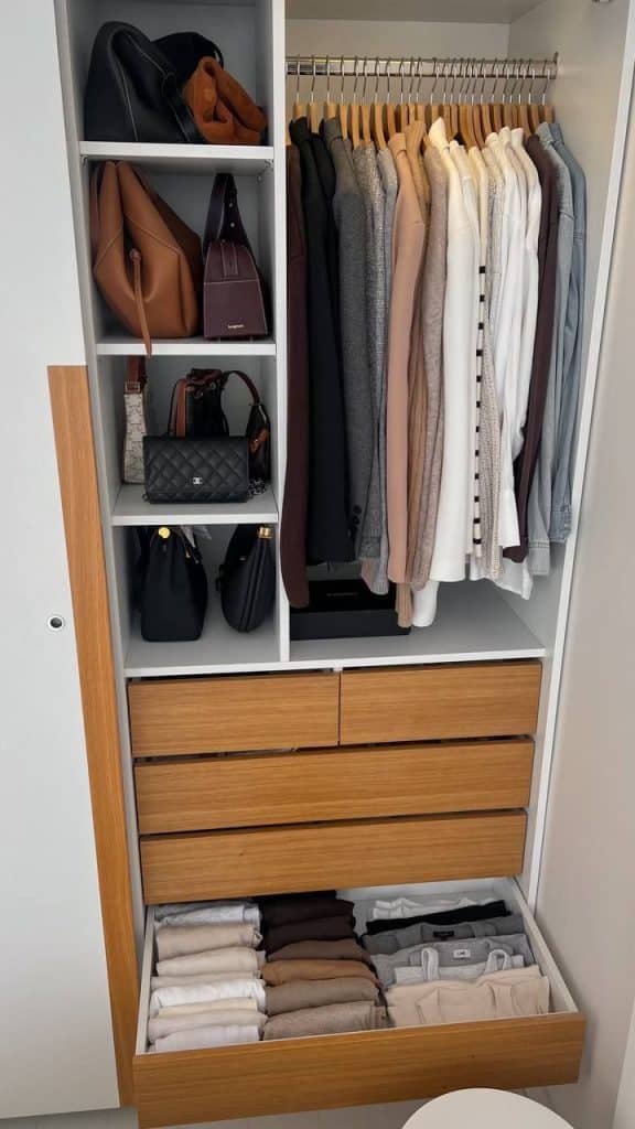 Built-in white closet with light wood drawers, one drawer open showing clothes stored using the vertical file folding method.