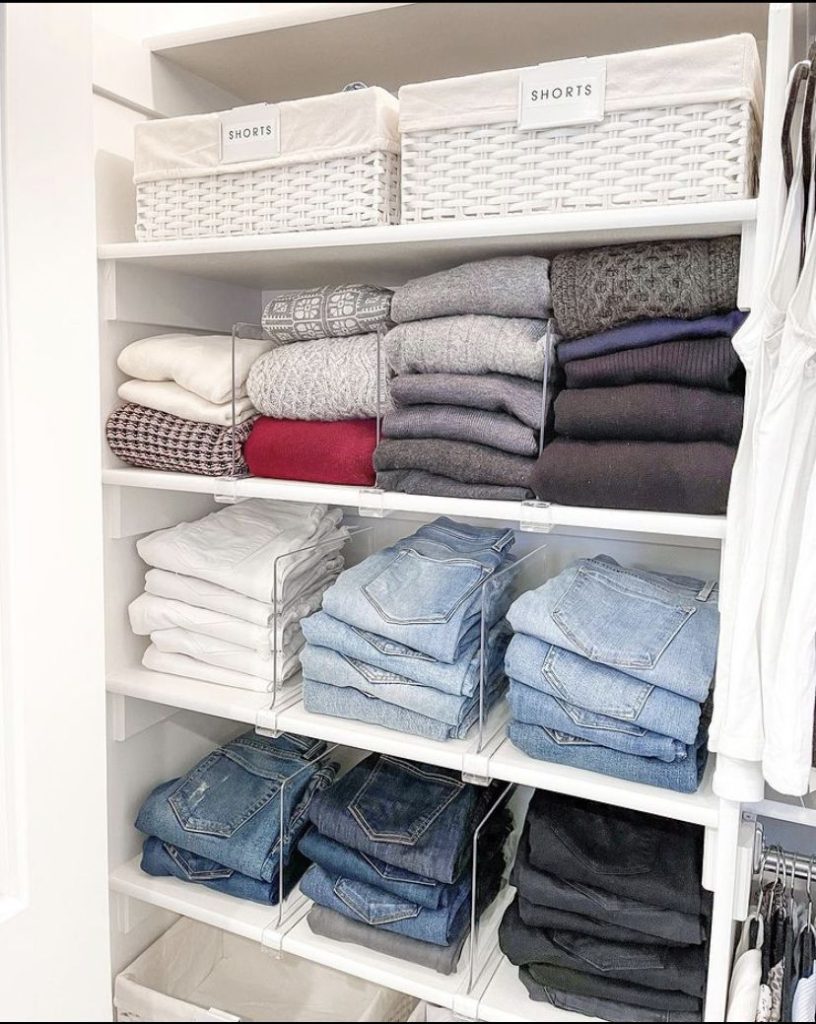 White closet shelving organizing folded jeans and sweaters using clear acrylic dividers for neat, separated stacks.