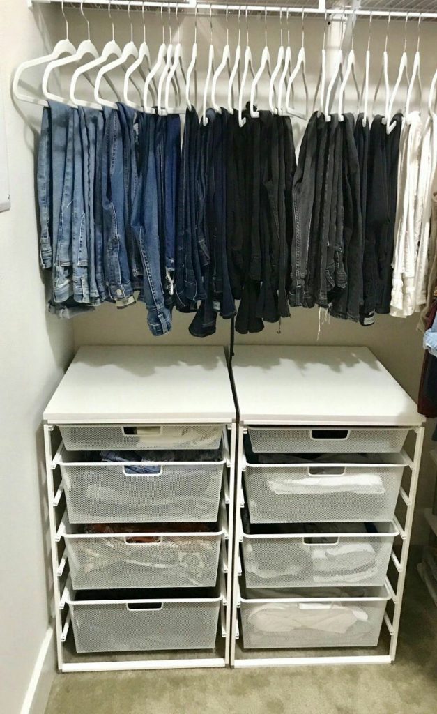 Closet area with a high hanging rod for dark denim jeans above two white modular drawer units with mesh metal pull-out baskets.