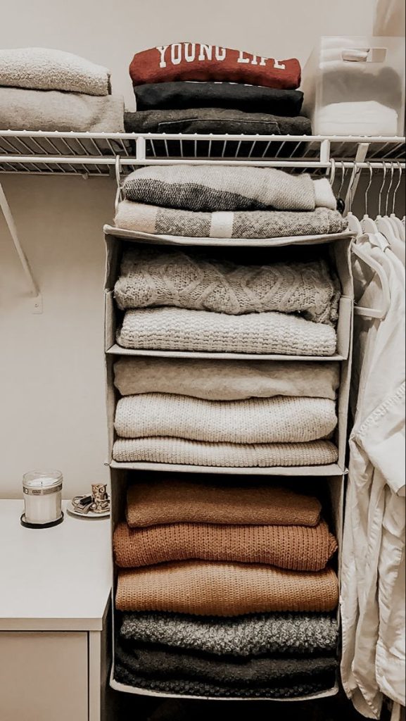 Close-up of vertical hanging fabric shelving unit filled with neatly folded cream and brown chunky knit sweaters.