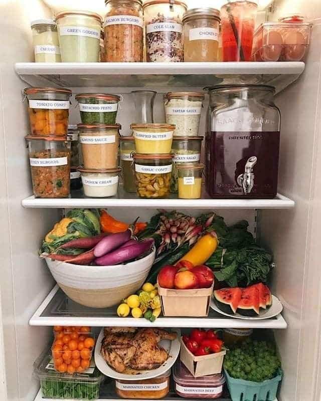 Large ceramic bowl filled with whole eggplants and radishes on a fridge shelf.