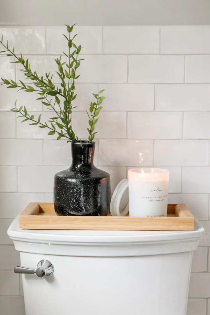 Minimalist toilet cistern decor with a light wood tray, a black speckled vase with a green sprig, and a white scented candle.