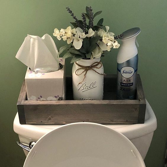 Functional toilet cistern decor featuring a wooden tray holding a tissue box, a Mason jar with faux flowers, and an air freshener spray.