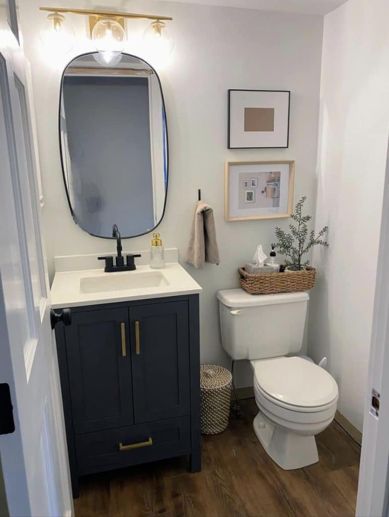 Sleek and modern small bathroom with dark navy vanity and black-framed mirror, showing a woven basket on the toilet cistern holding essentials.