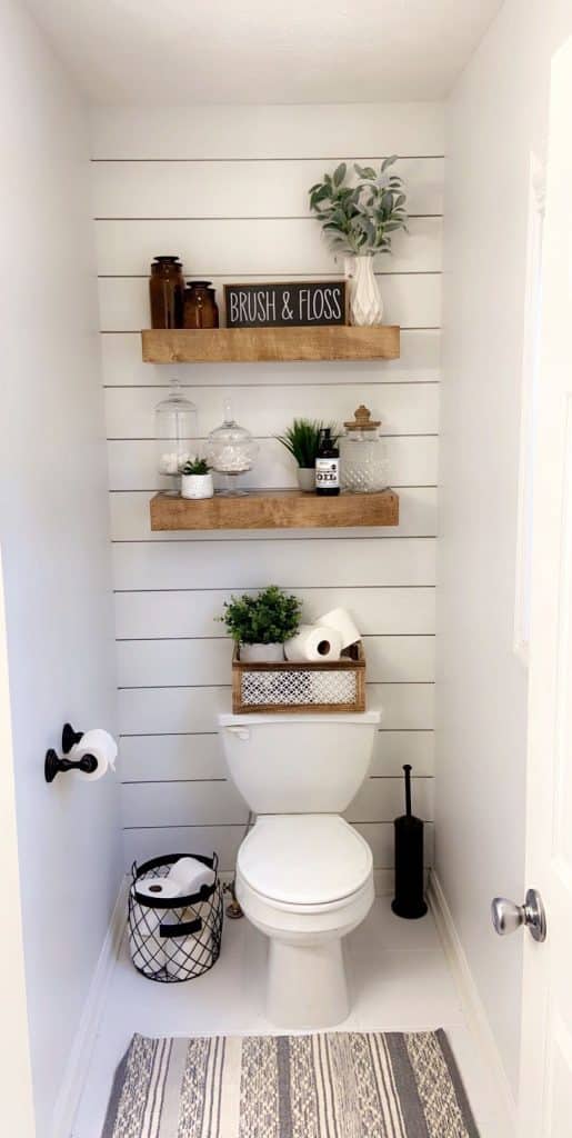 Full wall ship lap and vertical storage in a narrow bathroom, with three floating shelves and a small wooden crate on the toilet cistern.