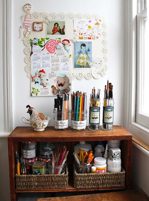 Glass preserve jars holding colored pencils and paintbrushes on a rustic wooden shelf next to a mood board.
