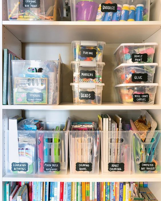 White shelves holding clear plastic bins with black chalkboard labels for different craft categories.
