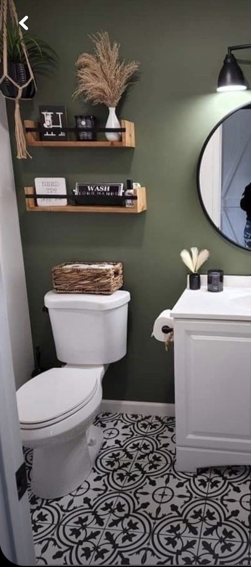 Small bathroom with wooden floating shelves styled with pampas grass in a white vase, a woven basket on the toilet tank, and small black signs on the shelf.