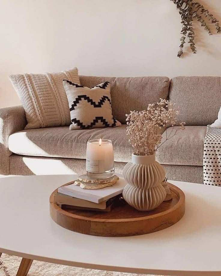 White round coffee table with a round wood riser tray holding a beige ribbed vase with dried baby's breath, a glass candle on stacked books, and a small gold scalloped dish.