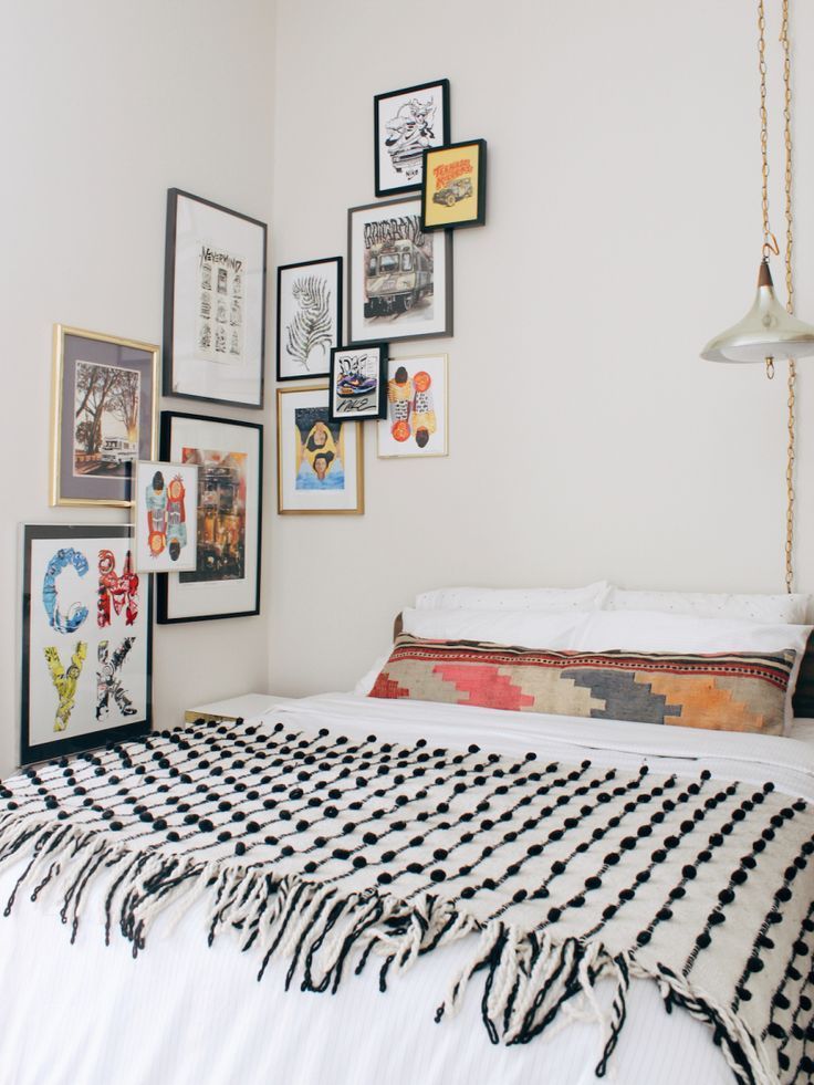 Eclectic bohemian bedroom with a colorful corner gallery wall of mixed framed art prints in black and gold frames, styled in a staggered organic arrangement that wraps from the wall beside the bed up toward the ceiling corner.